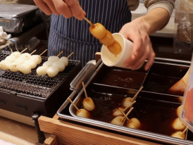 Vendor glazing mitarashi dango rice dumplings at a Tokyo street food stall