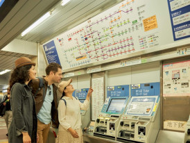 Travelers using ticket machines and reading a subway map in a Japanese train station