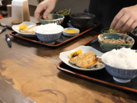 Traditional Japanese breakfast with grilled fish, rice, miso soup, and side dishes served on trays at a local restaurant
