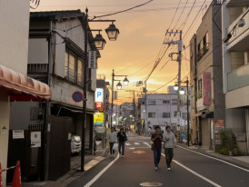 Quiet Tokyo neighborhood street at sunset with pedestrians walking past local shops