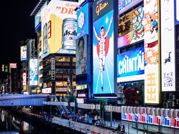 Street scene in Dotonbori with neon signs reflecting in the canal.