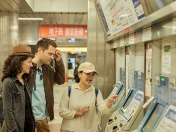 Host pointing to a train map showing the route between Osaka and Kyoto while travelers look on with interest Host pointing to a train map showing the route between Osaka and Kyoto while travelers look on with interest