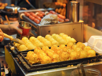 A sizzling pan of takoyaki being turned by a vendor A sizzling pan of takoyaki being turned by a vendor