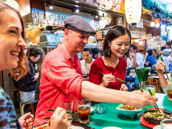 A local host and guest sharing street food from a small vendor stall. A local host and guest sharing street food from a small vendor stall.