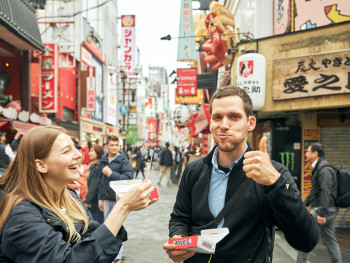 The author smiling while eating takoyaki on a busy Osaka street, looking genuinely happy and content. The author smiling while eating takoyaki on a busy Osaka street, looking genuinely happy and content.