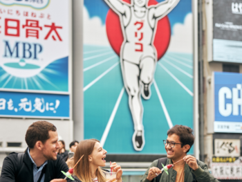Local residents and visitors sharing street food in Dotonbori, representing cultural exchange. Local residents and visitors sharing street food in Dotonbori, representing cultural exchange.