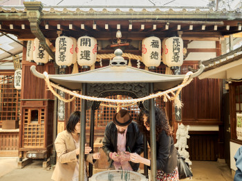 A small group of travelers discovering a tucked-away shrine hidden in a quiet Osaka alley, surrounded by stone lanterns and lush greenery. A small group of travelers discovering a tucked-away shrine hidden in a quiet Osaka alley, surrounded by stone lanterns and lush greenery.