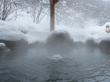 An outdoor hot spring surrounded by snow-covered rocks and bare winter trees An outdoor hot spring surrounded by snow-covered rocks and bare winter trees