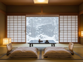 A traditional ryokan room with tatami mats and futon bedding, snow visible through paper screen windows A traditional ryokan room with tatami mats and futon bedding, snow visible through paper screen windows
