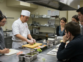 Students learning sushi preparation techniques from a master chef in a professional kitchen classroom setting. Students learning sushi preparation techniques from a master chef in a professional kitchen classroom setting.