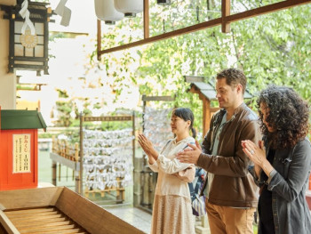 Host demonstrating proper etiquette at a traditional shrine while travelers observe respectfully. Host demonstrating proper etiquette at a traditional shrine while travelers observe respectfully.