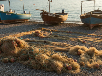 Traditional fishing boats pulled up on a pebbly beach with nets drying in the foreground Traditional fishing boats pulled up on a pebbly beach with nets drying in the foreground
