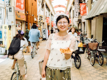 Host handing guest takoyaki in street market Host handing guest takoyaki in street market