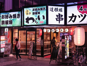 Osaka alleyway with food stalls lit up by warm lanterns, crowds gathering as evening approaches Osaka alleyway with food stalls lit up by warm lanterns, crowds gathering as evening approaches