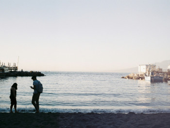 Pebble beach with clear water and small boats near seaside cafes Pebble beach with clear water and small boats near seaside cafes