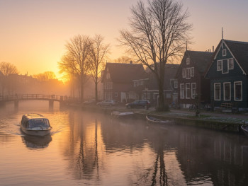 Whisper boat gliding past thatched cottages at sunrise mist Whisper boat gliding past thatched cottages at sunrise mist