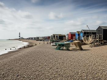 Shingle beach with fishing huts and a lighthouse at Dungeness Shingle beach with fishing huts and a lighthouse at Dungeness