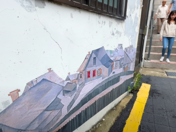 A wall Ihwa Mural Village painted with a mural of a small town while people pass by A wall Ihwa Mural Village painted with a mural of a small town while people pass by