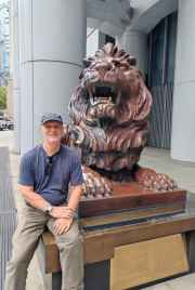 Man seated beside lion statue outside HSBC Main Building, Hong Kong.