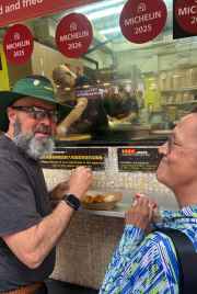 Tourist savoring street food delicacies outside a bustling Hong Kong eatery.