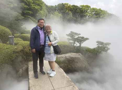 Two people standing on a walkway in a foggy Japanese garden.