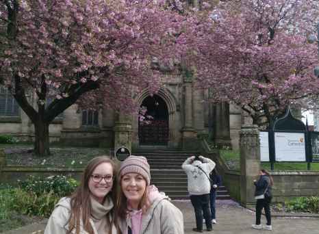 Two people standing in front of Manchester Cathedral with cherry blossoms.