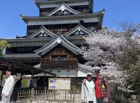 People stand in front of Hiroshima Castle with cherry blossom trees in the background.