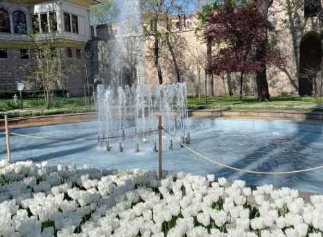 Fountain and tulips in Gülhane Park, Istanbul, with historical building in the background.