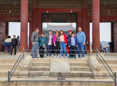 Family standing in front of traditional gate at Gyeongbokgung Palace.