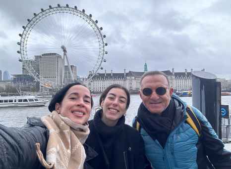 Visitors standing near the River Thames with the London Eye behind.