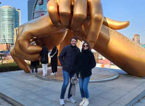 Two people stand in front of the Golden Hand sculpture in Gangnam, Seoul.
