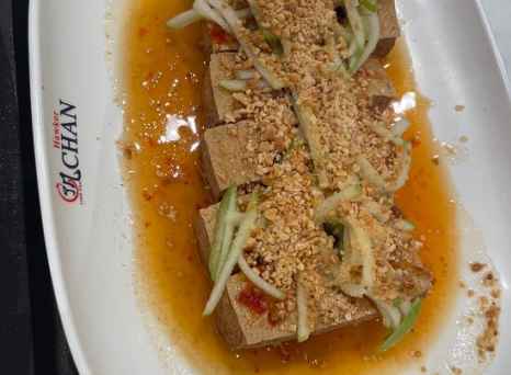 Plate of tofu topped with chopped nuts and sliced vegetables at Hawker Chan.