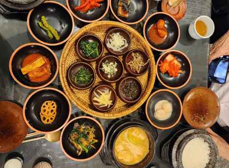 Korean banchan dishes arranged on a gray stone table with rice and tea.