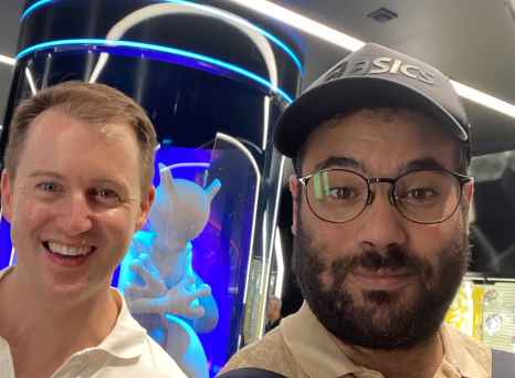 Individuals in a technologically themed room with curved glass and neon lights.