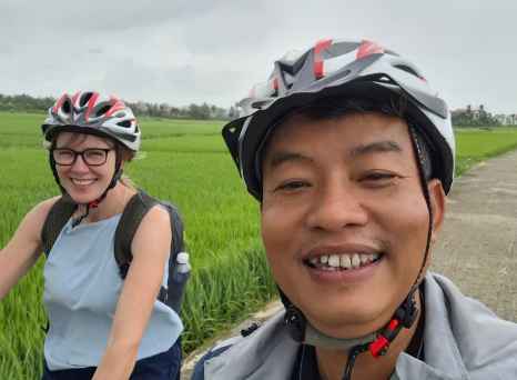 Man and woman cycling on a path with green fields surrounding them.