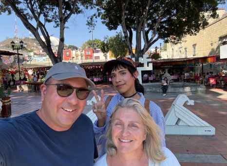 Three people posing at a Mexican square with shops in the background.