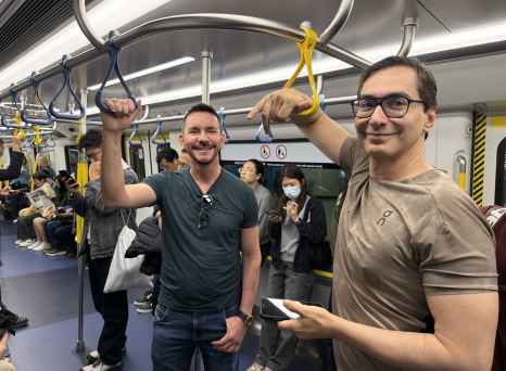 Two men standing in a subway train holding onto the handrails.