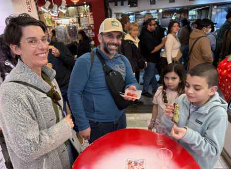 A family enjoys snacks at a table inside a busy Kyoto market area.