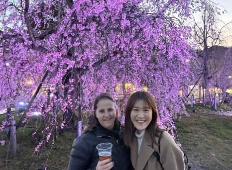 Two people stand in front of illuminated cherry blossoms at night.