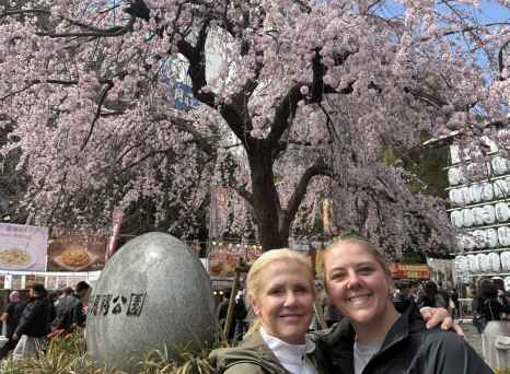 Two people pose in front of a cherry blossom tree in Tokyo.