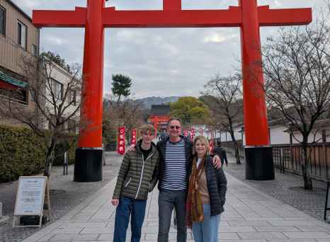 Three people standing in front of a large red torii gate at Fushimi Inari Shrine.