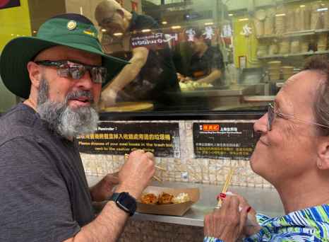 Tourist savoring street food delicacies outside a bustling Hong Kong eatery.
