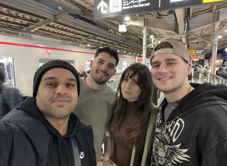 A joyful group selfie beneath bright station signs in Tokyo.