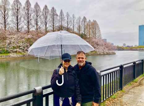 A couple enjoys cherry blossoms under a shared umbrella in Osaka.