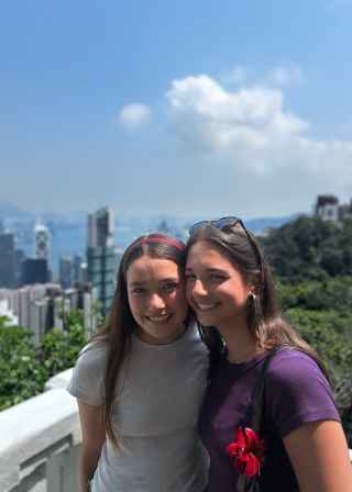 Two friends share a smile with Hong Kong's skyscrapers behind them.