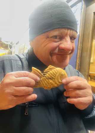 Tourist holds up a fish-shaped pastry with a playful grin.