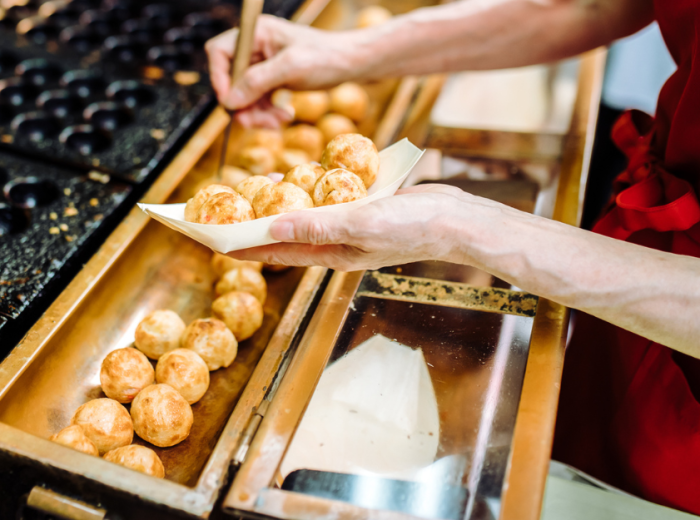 A close-up of sizzling takoyaki being turned on a street grill in Dotonbori.