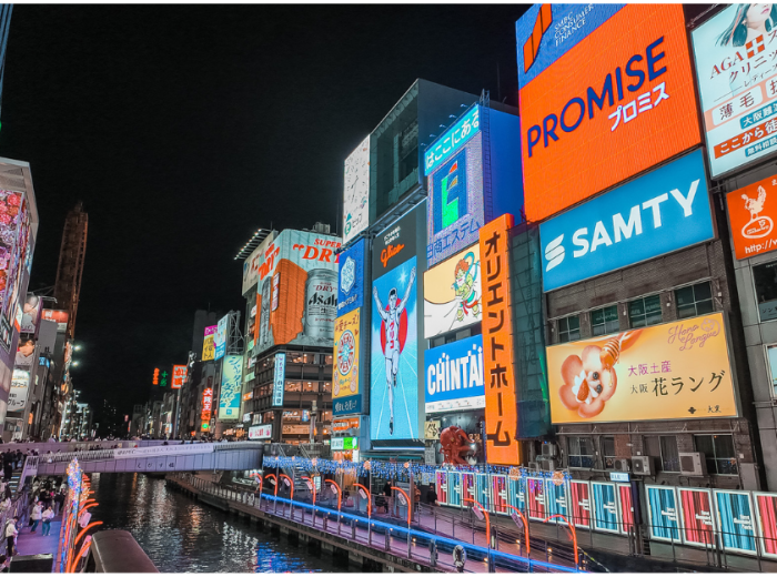 Bustling evening street scene in Dotonbori with neon signs and food vendors.