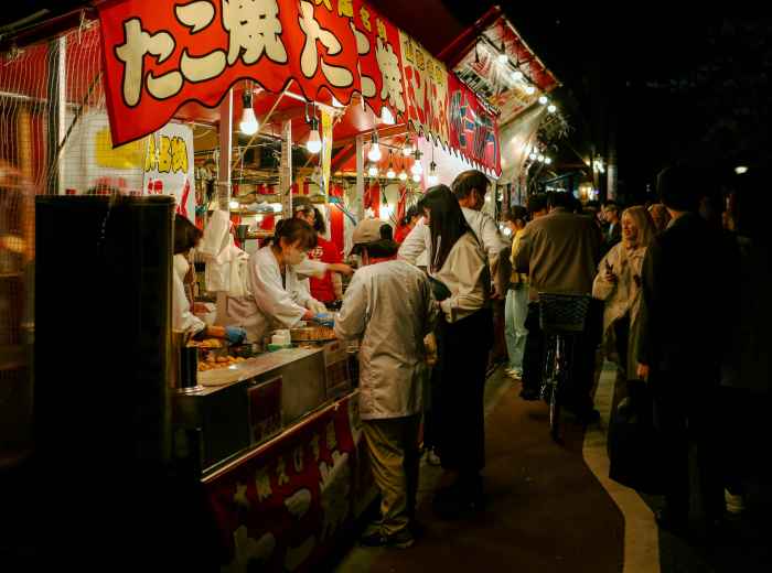 Multiple takoyaki vendors lined up along Dotonbori street with bright signage. Photo by HANVIN CHEONG on Unsplash