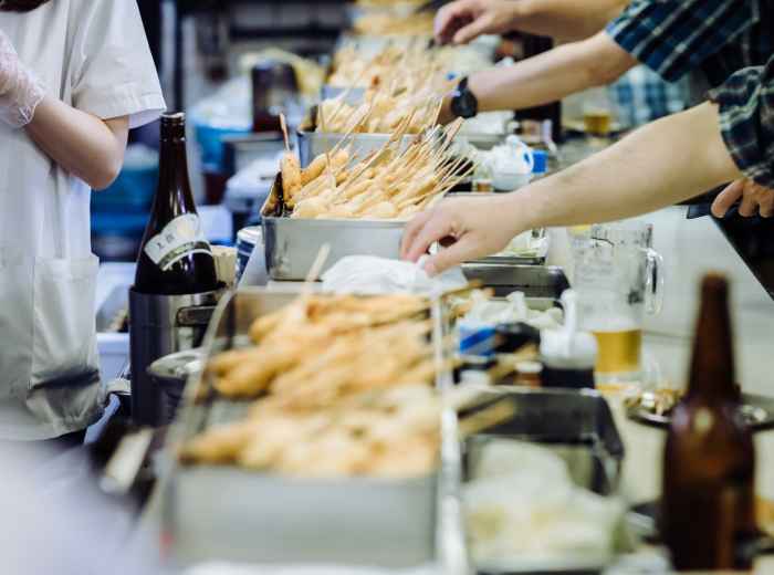 Traditional kushikatsu restaurant with customers standing at outdoor counters.
